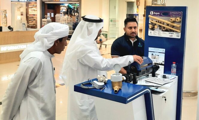 Moosa-Daly representative explaining a plumbing component to two Emirati visitors at Madinat Zayed event.
